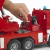A child's hand is shown operating a mechanism on a red toy fire engine. Náhled obrázku produktu