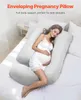 A pregnant woman is lying on a bed, using a U-shaped pregnancy pillow. Podgląd zdjęcia produktu