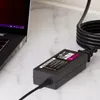 A laptop power adapter and its power cord are shown on a marble surface next to a laptop. Podgląd zdjęcia produktu