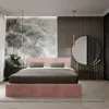 A bedroom scene featuring a pink upholstered bed, a dresser with flowers, and a large round mirror. Náhľad obrázku produktu