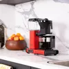 A red coffee maker sits on a marble countertop next to a bowl of fruit. Náhled obrázku produktu