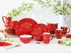 A red and white polka dot dinnerware set arranged on a table with a white pitcher and greenery. Produktbild-Vorschau