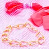 A gold chain bracelet is laid out on a pink knitted surface, with a spool of red embroidery thread and a piece of pink fabric in the background. Podgląd zdjęcia produktu