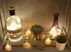 A collection of decorative items including bottles with fairy lights, succulents in pots, and LED tealights arranged in a rustic wooden crate. Náhled obrázku produktu