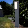 A modern outdoor lamp post is illuminated in a garden at dusk, with a house and trees in the background. Anteprima dell’immagine prodotto