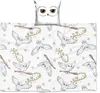A white pillow with a drawing of owl eyes and a white blanket with a repeating pattern of white owls flying with letters and broomsticks. Produktbild-Vorschau