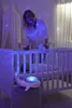 A woman is standing next to a crib, looking down at a baby. A whale-shaped night light is on a stool next to the crib. Anteprima dell’immagine prodotto