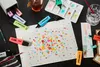 A collection of STABILO BOSS ORIGINAL highlighters scattered around a piece of paper with colorful dots, along with art supplies like brushes, a palette, and a glass of water. Anteprima dell’immagine prodotto