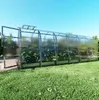 A long, clear greenhouse with plants inside, set up on a grassy lawn under a clear blue sky. Produktbild-Vorschau
