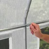 A close-up view of a person's hand holding a metal bar on a greenhouse frame, with the white transparent plastic sheeting visible. Produktbild-Vorschau