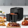 A black air fryer is shown in a kitchen setting, with various cooked foods displayed around it. Produktbild-Vorschau