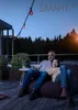 A couple relaxing on a beanbag chair on a balcony at dusk, with string lights overhead. Produktbild-Vorschau