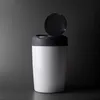 A white container with a black lid, partially open, against a gradient gray and black background. Voir les images du produit