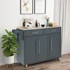 A kitchen cart with a wooden top, two drawers, and two cabinet doors, placed in a room with a plant and artwork on the wall. Produktbild-Vorschau