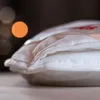 A close-up of a white duvet with visible stitching and layers, with blurred bokeh lights in the background. Produktbild-Vorschau