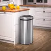 A stainless steel sensor trash can is placed next to a kitchen island with a pitcher of orange juice and oranges on it. Náhľad obrázku produktu