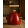 A red enamel kettle sits on a wooden table in a rustic kitchen setting. Podgląd zdjęcia produktu