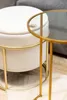 A close-up shot of a cream-colored ottoman with a gold metal frame, next to a gold metal side table with a glass top. Náhled obrázku produktu