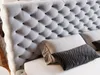 A close-up view of a tufted headboard and pillows on a bed. Produktbild-Vorschau