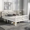 A white wooden bed frame with a headboard and footboard, set up in a bedroom with a rug and a nightstand. Produktbild-Vorschau