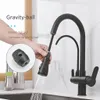 A hand is shown pulling out the spray head of a black kitchen faucet, with water spraying from it. A close-up inset shows the gravity ball component. Náhľad obrázku produktu