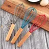 Three whisks with wooden handles are arranged diagonally on a wooden cutting board. Produktbild-Vorschau