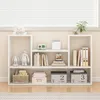 A white bookshelf filled with books, decorative items, and storage boxes, placed in front of a window with blinds. Náhľad obrázku produktu