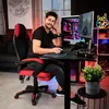 A man is sitting in a gaming chair at a desk with a computer, playing a game. Produktbild-Vorschau