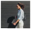 A woman walks past a striped wall, holding a tablet case. Náhľad obrázku produktu