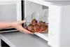 A hand is placing a glass dish of meatballs and vegetables into a microwave. Anteprima dell’immagine prodotto