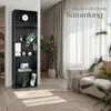 A modern living room with a black bookshelf filled with decorative items and books, next to a sofa and a large plant. Náhled obrázku produktu