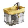 A pet drinking fountain with water flowing from a silver spout into a yellow-topped, clear reservoir. Produktbild-Vorschau