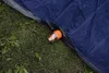 A close-up view of an inflatable mattress with an orange pump attached to its valve, resting on grass. Podgląd zdjęcia produktu