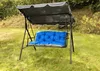 A garden swing with a blue cushion is set up on a grassy lawn. Produktbild-Vorschau