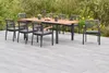 An outdoor dining set with a table and chairs on a patio, surrounded by greenery and flowers. Náhled obrázku produktu