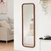 A full-length mirror with a brown frame is shown leaning against a white wall in a living room setting. A sofa and a small side table with a vase of flowers are visible in the reflection. Voir les images du produit