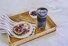 A breakfast tray with toast, berries, and a travel mug on a bed. Podgląd zdjęcia produktu