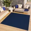 An outdoor patio scene with a navy blue rug, beige sofas, and a coffee table. Produktbild-Vorschau