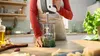 A person is using a hand blender to make pesto in a kitchen. Produktbild-Vorschau