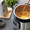 A close-up shot of a multi-cooker with macaroni and cheese being stirred with a wooden spoon, with a grater and block of cheese in the background. Náhled obrázku produktu