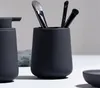 A black ceramic toothbrush holder with makeup brushes inside, next to a black soap dispenser. Produktbild-Vorschau