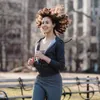 A woman is running in a park with buildings in the background. Produktbild-Vorschau