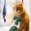 An orange cat is looking at a toy fish dangling in front of it, while a handheld vacuum cleaner is being held near the cat's body. Produktbild-Vorschau
