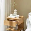 A wooden nightstand with an open drawer, a vase with flowers, a candle, and a mug on top. Produktbild-Vorschau