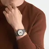 A person wearing a brown sweater and a silver watch. Produktbild-Vorschau
