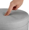 A hand is pressing down on the padded top of a round ottoman. Podgląd zdjęcia produktu