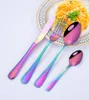 A set of rainbow-colored cutlery is arranged on a white surface, with a plate of spaghetti in the background. Produktbild-Vorschau
