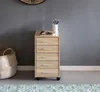 A small wooden filing cabinet with five drawers on wheels, placed against a gray wall next to a woven basket. Produktbild-Vorschau