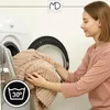 A woman is putting a beige blanket into a washing machine. Anteprima dell’immagine prodotto