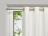 A white curtain is hanging from a silver curtain rod in front of a window with green trees visible outside. Produktbild-Vorschau